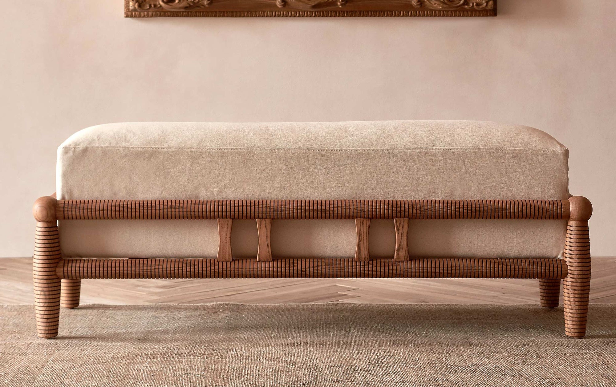 Gio Dining Bench in a Heritage Ash wood frame with Cotton Canvas Beach Walk slipcover, placed on top of a rug