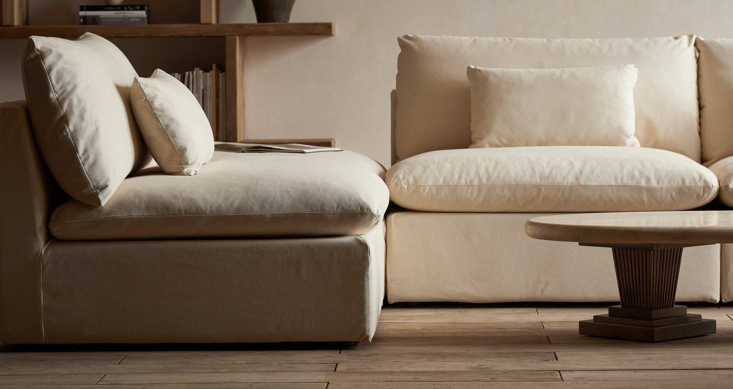 Close up view of an Aria Sectional in Cotton Canvas Beach Walk around the Cordelia Coffee Table in Galata Travertine and Heritage Pine