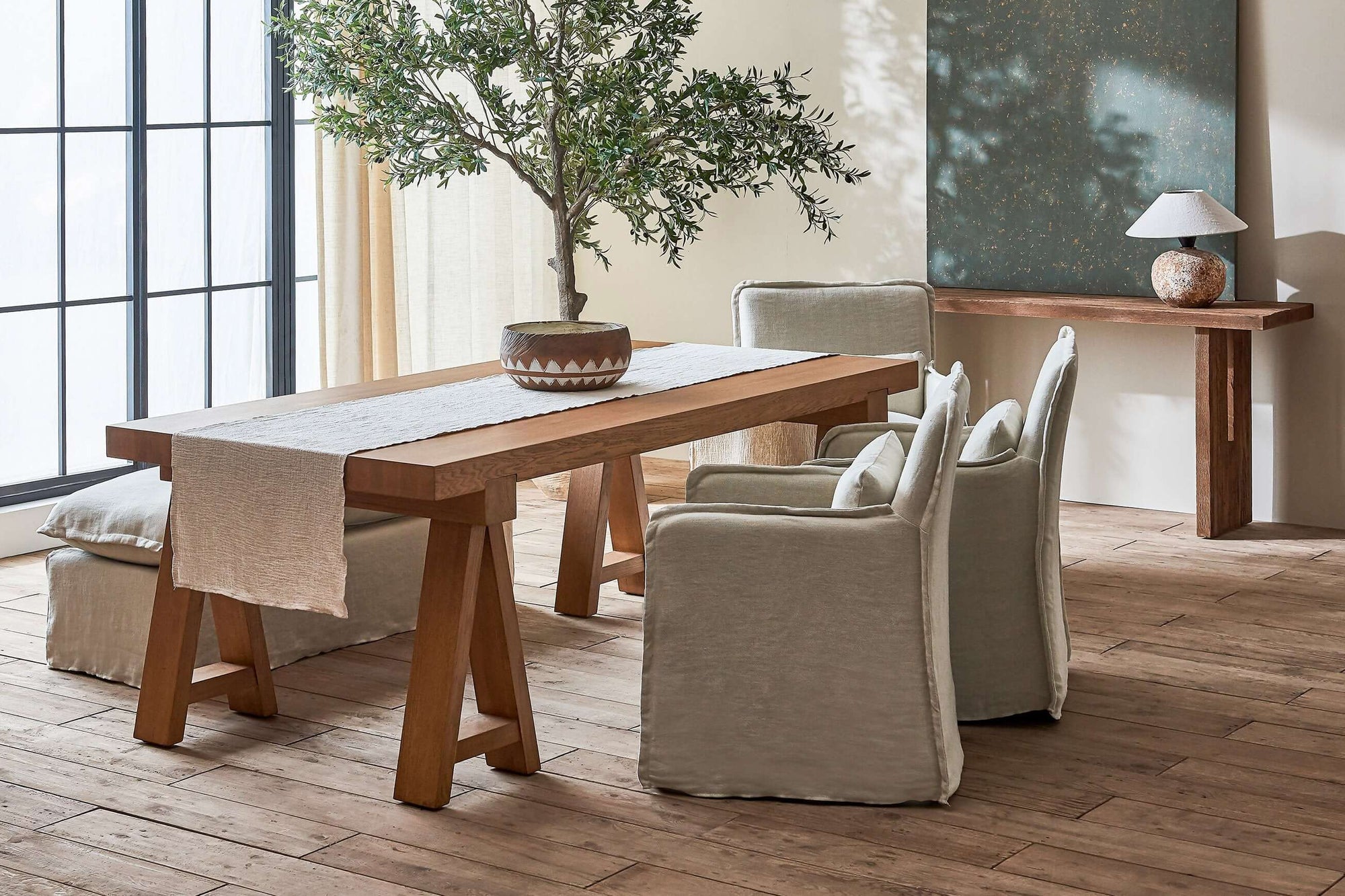 Two Melo Dining Chairs in Jasmine Rice, a light warm greige Medium Weight Linen, sitting at a Rylance Dining Table with a Neva Dining Bench
