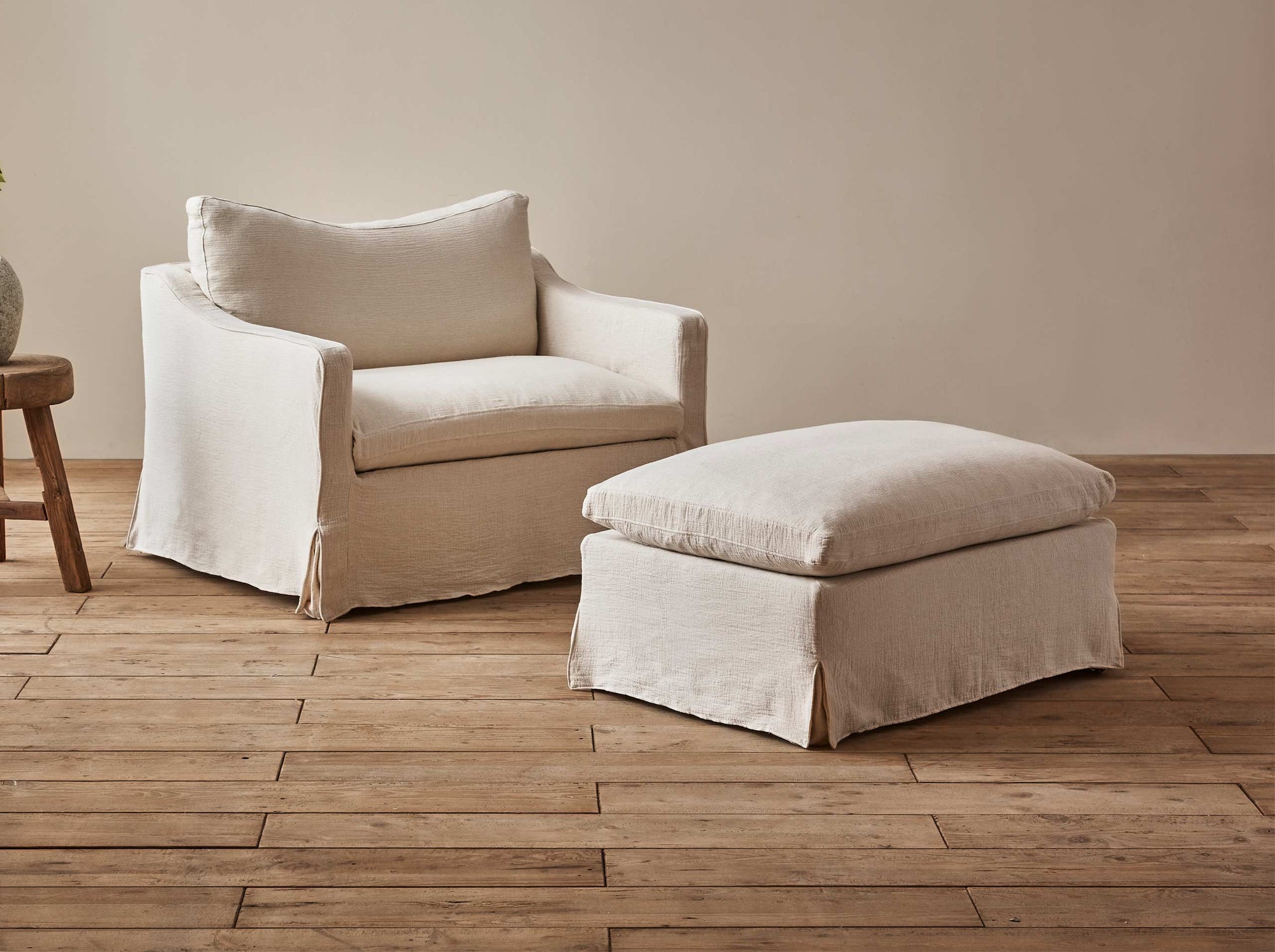 Amelia Chair Ottoman in Corn Silk, a light beige Washed Cotton Linen, placed in a room with the Amelia Chair and a plant on a stool