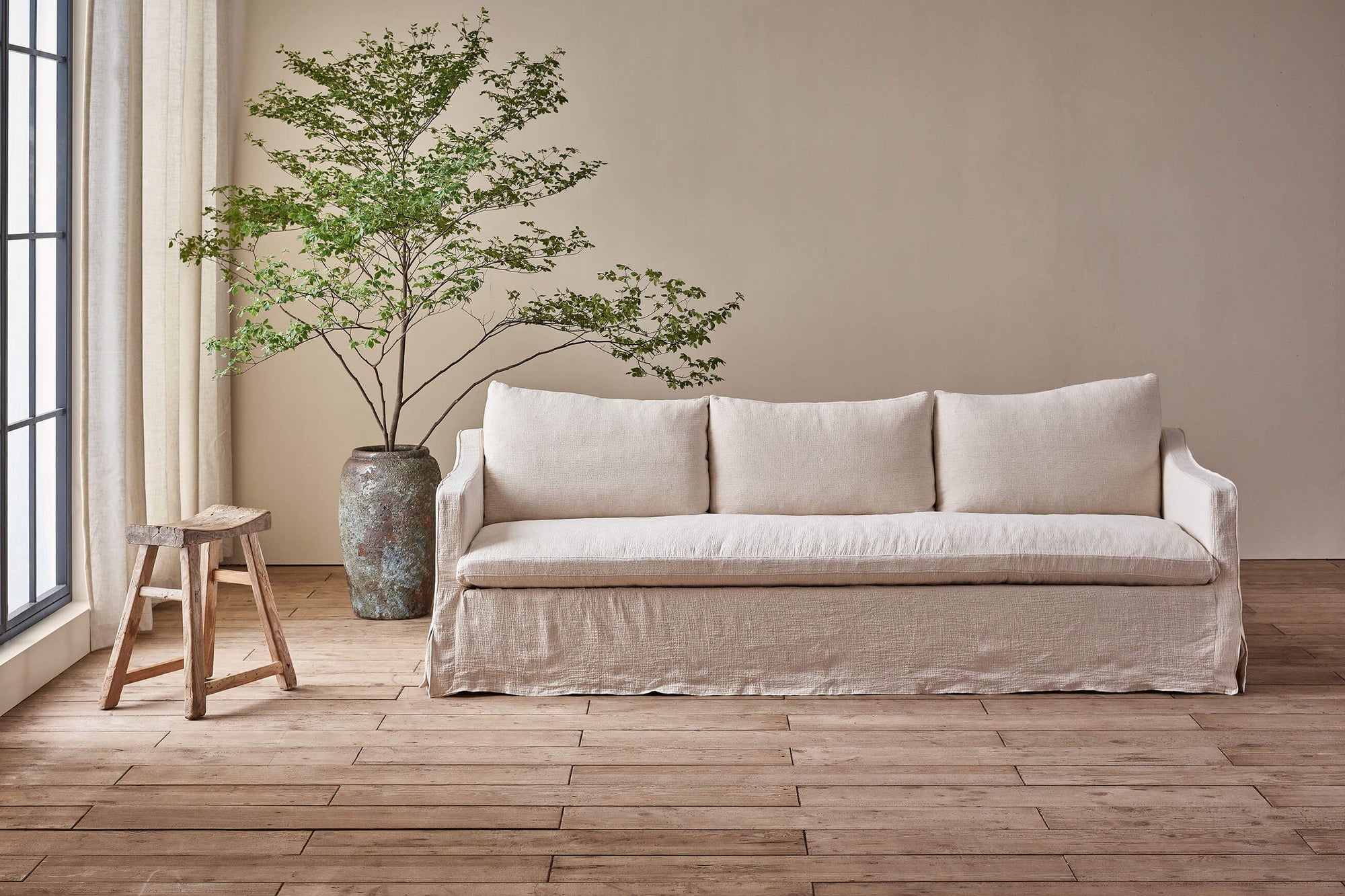 Amelia 96" Sofa in Corn Silk, a light beige Washed Cotton Linen, in front of a large potted plant