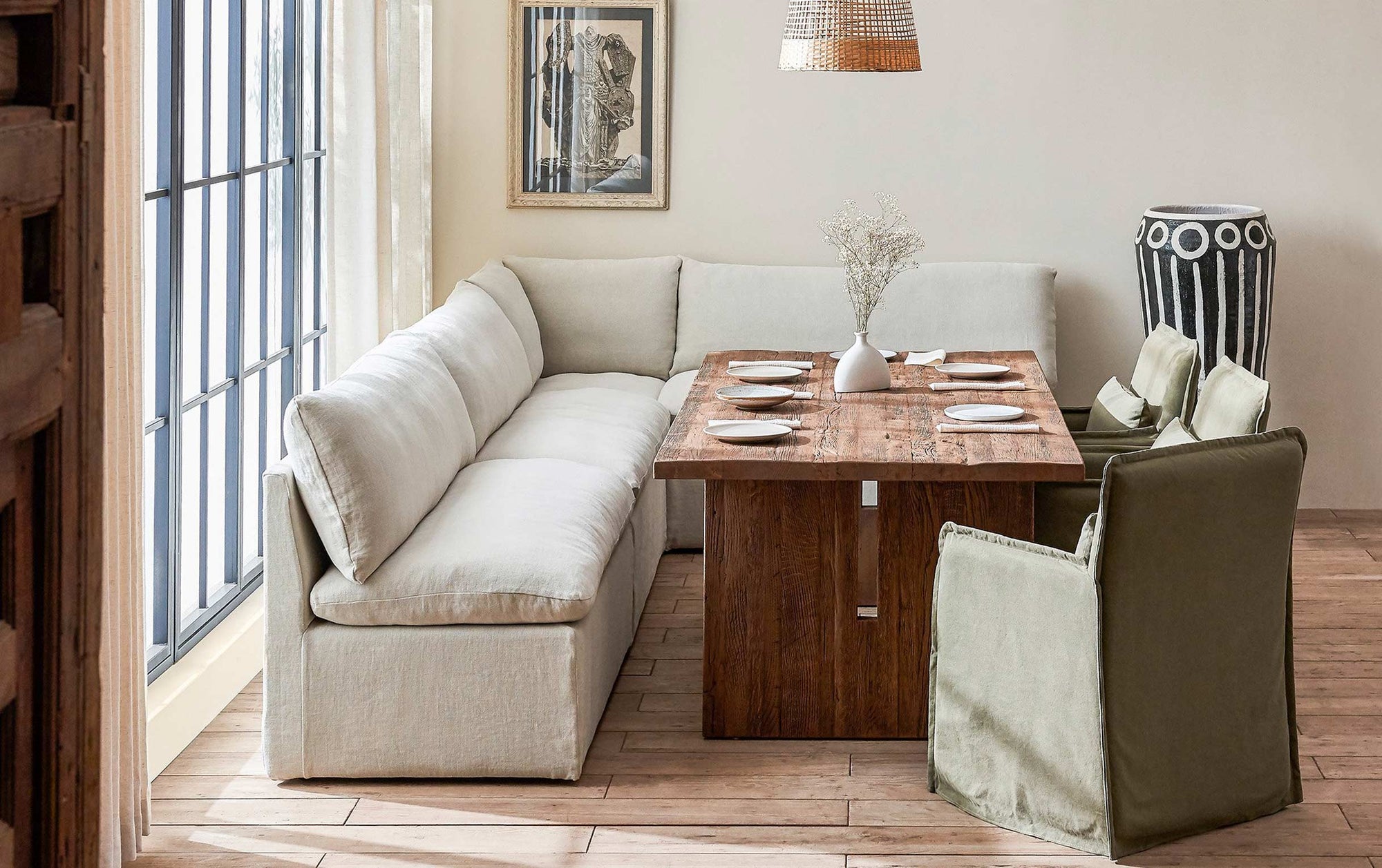 Aria Banquette in Warm Oatmeal, a light warm beige Medium Weight Linen, placed in a room by a window, surrounding the Kai Dining Table and three Melo Dining Chairs