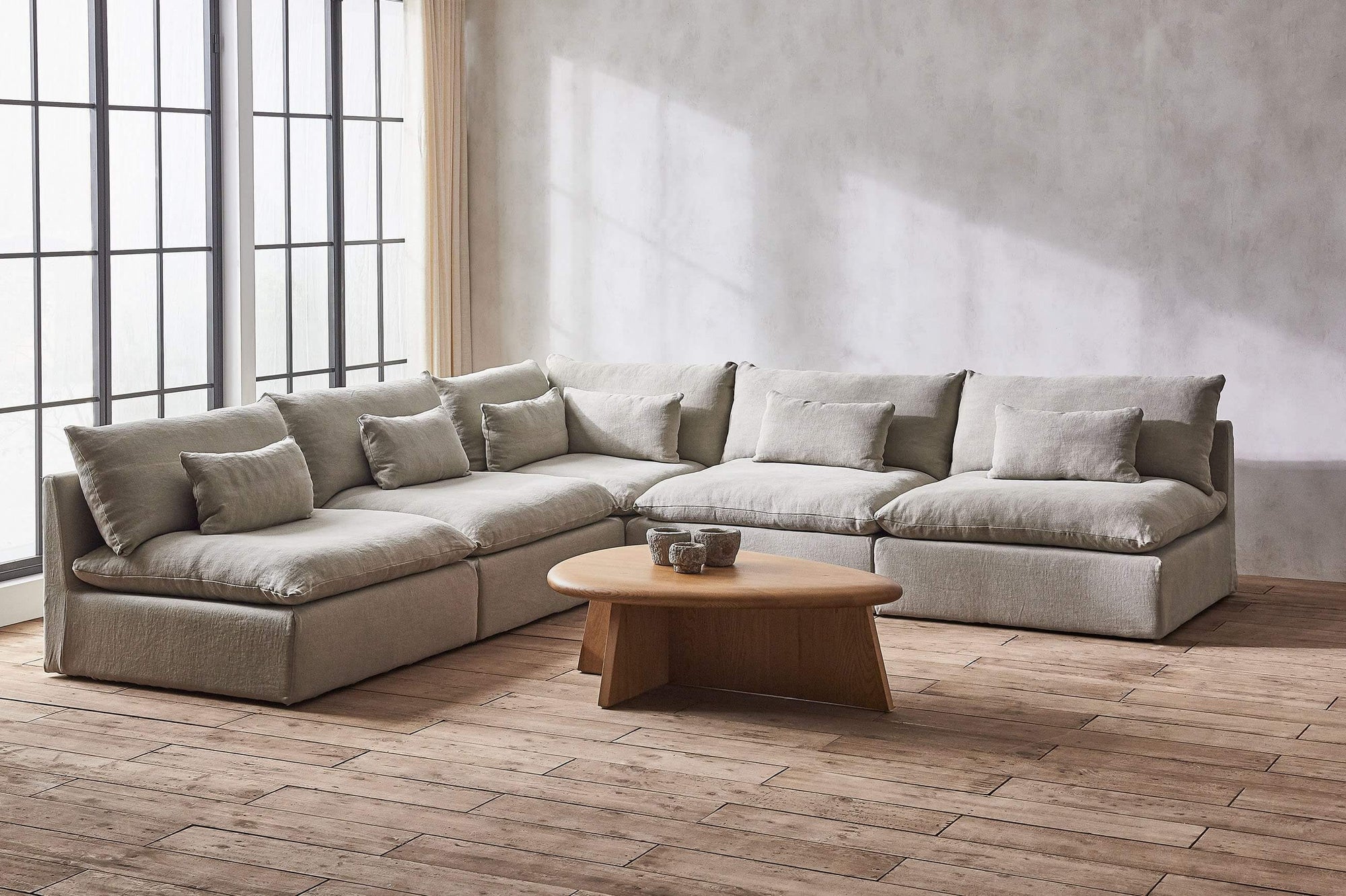 Aria Corner Sectional Sofa in Jasmine Rice, a light warm greige Medium Weight Linen, placed in a room with a decorrated Amina Coffee Table