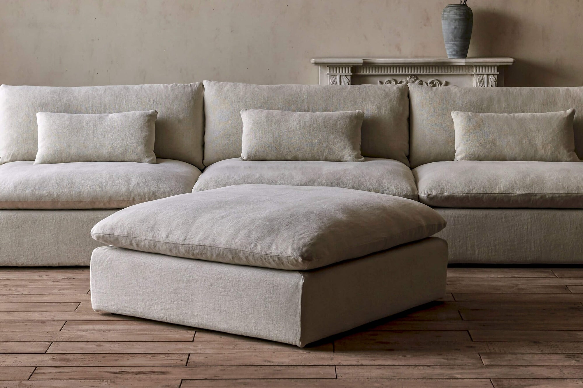 Aria Grande Ottoman in Warm Oatmeal, a light warm beige Medium Weight Linen placed in a room with Aria Grande Chaise Sectional in the background