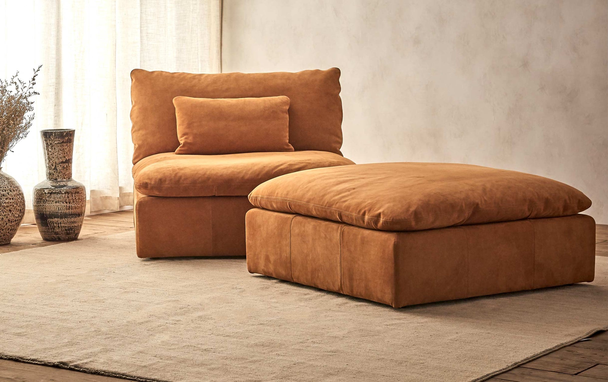 Aria Leather Ottoman in Sunset Canyon, a cognac brown Meridian Leather placed on a beige rug in front of the Aria Leather Chair