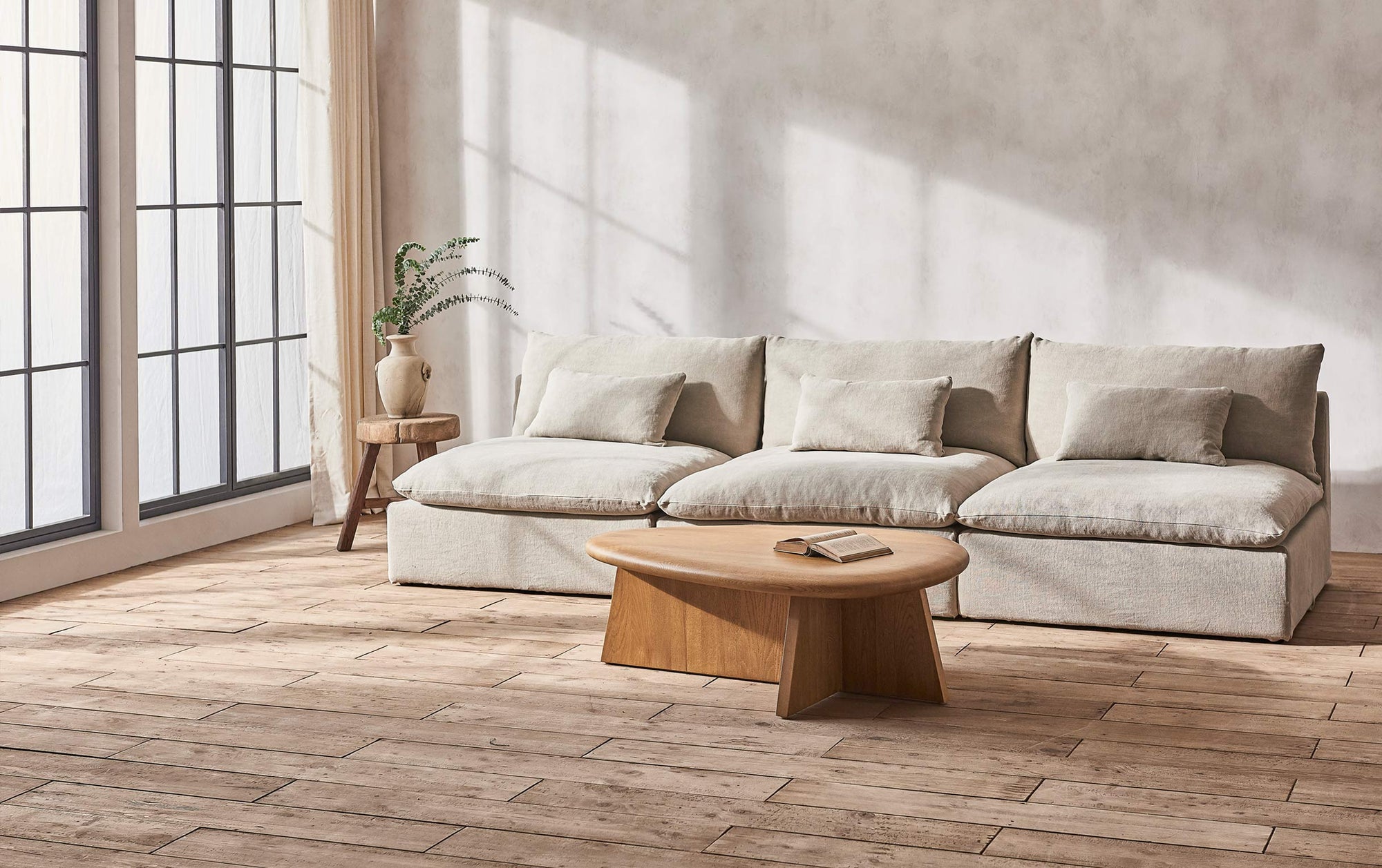 Aria Sectional Sofa in Jasmine Rice, a light warm greige Medium Weight Linen, placed in a sunlit room beside the Amina Coffee Table