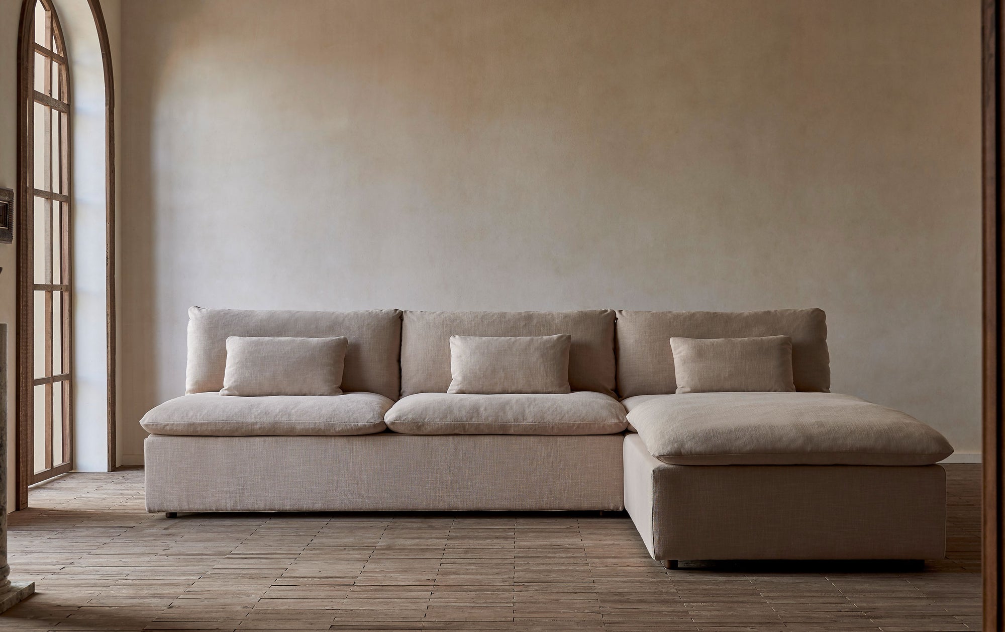 Aria Sleeper Chaise Sectional in Golden Reed, a sandy brown Recycled Poly Linen, sitting against a beige wall