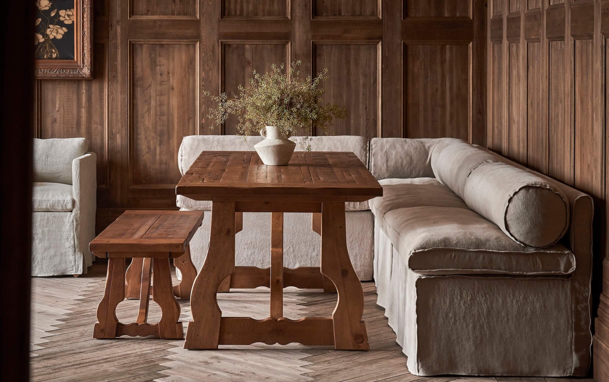 Camino Banquette in Cracked Pepper, a medium grey-beige Light Weight Linen placed with a Leona Dining Bench around a Leona Dining Table holding a vase of flowers