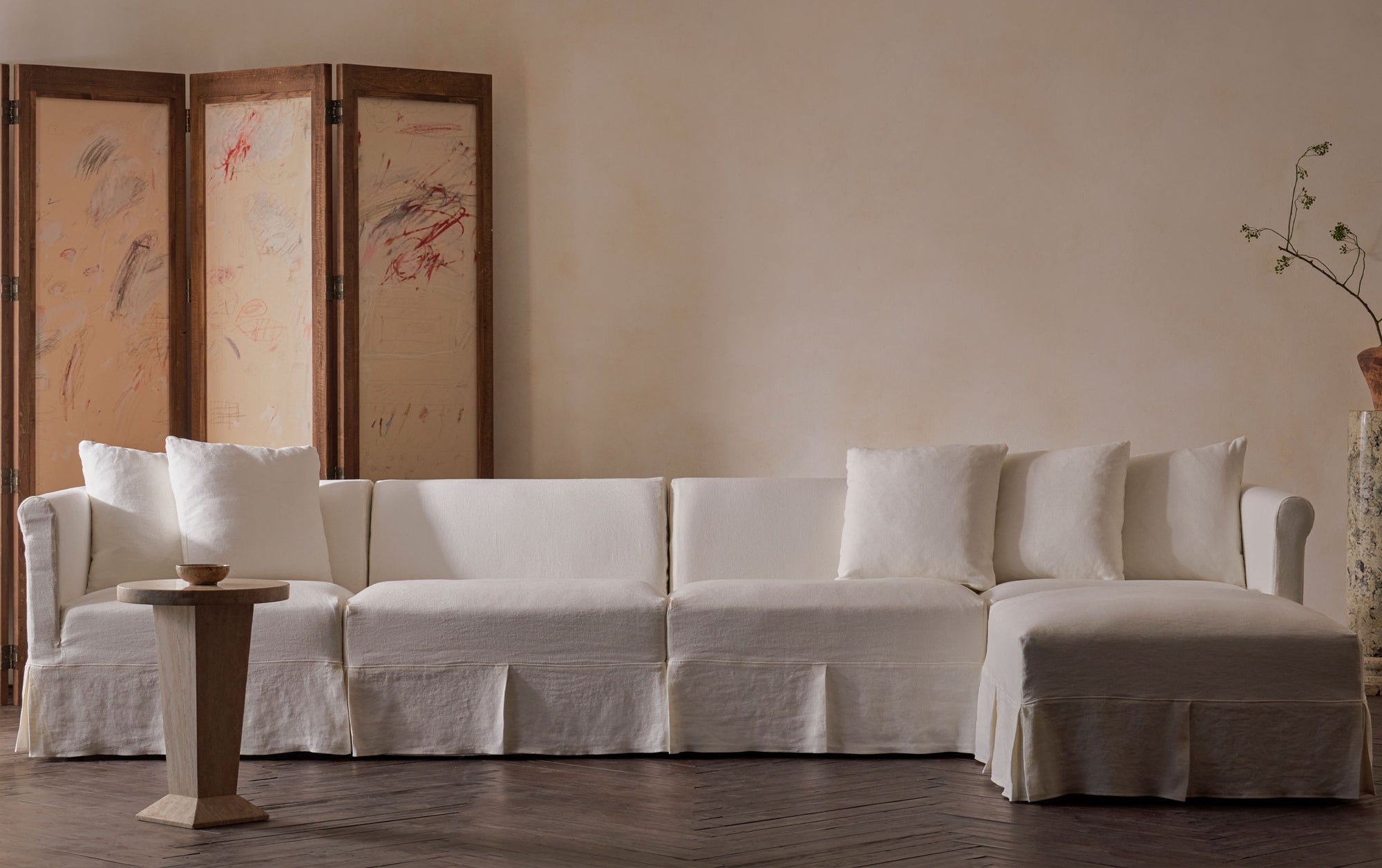 Dalia 5pc Chaise Sectional in Water Lily, a white Light Weight Linen with warm undertones, placed in a room decorated with a folding screen and a stone side table