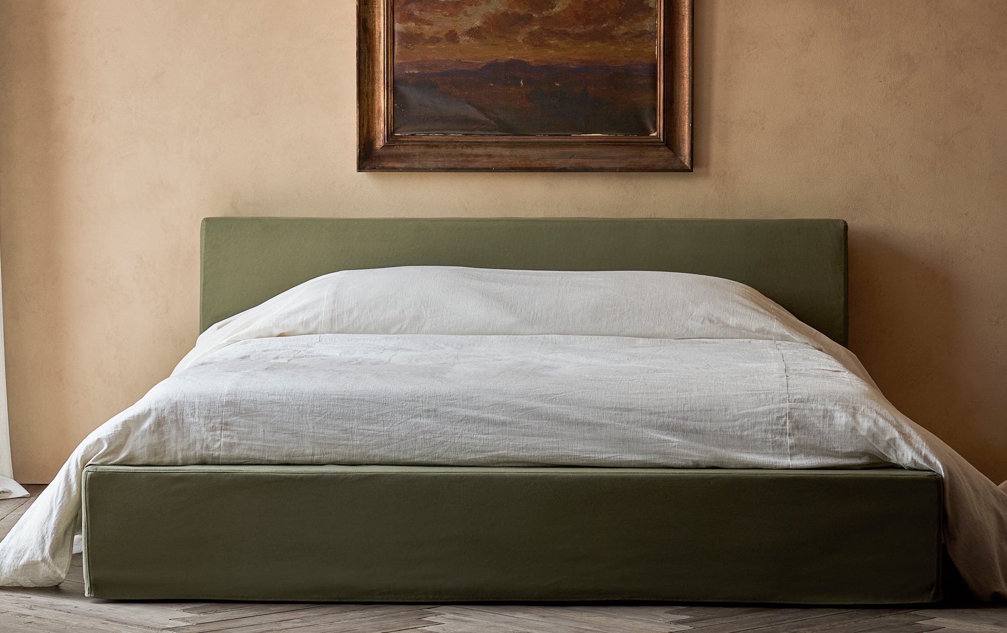 Devyn California King Bed in Quiet Sage, an earthy green Cotton Canvas, placed in a sunlit room with a scenic painting hanging on the wall