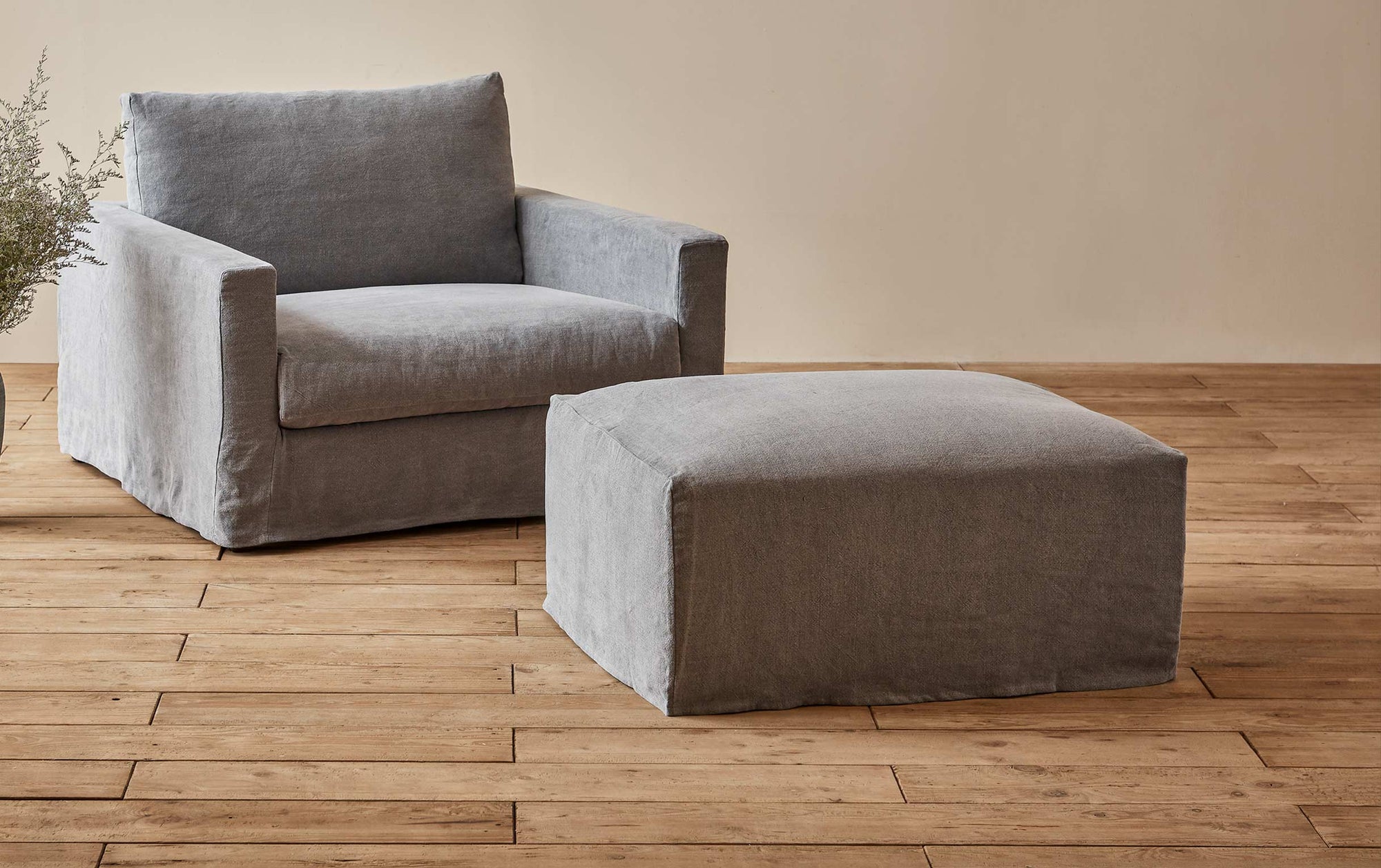 Devyn Chair and Ottoman in Ink Cap, a medium cool grey Light Weight Linen, placed in a sunlit room next to a plant
