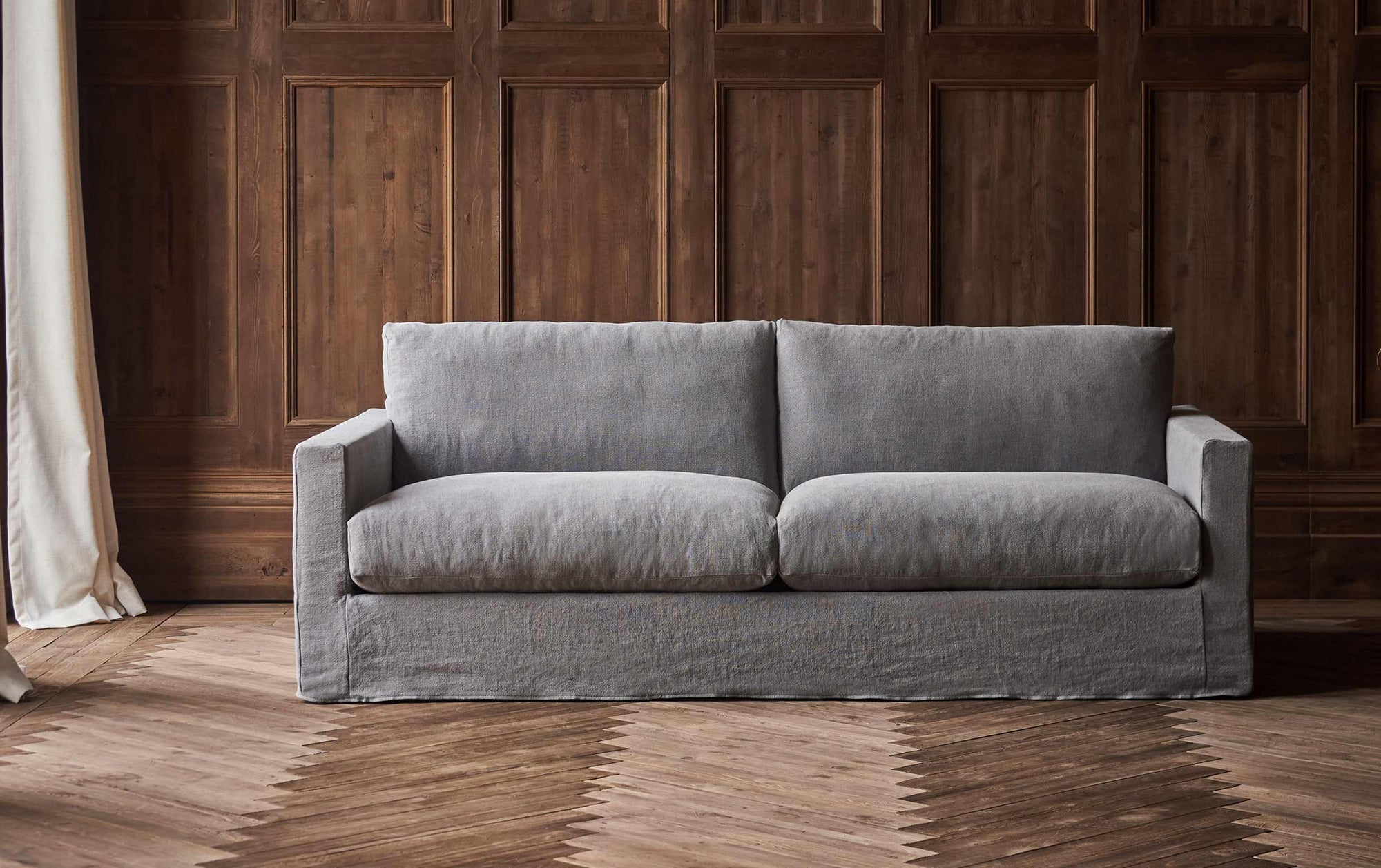 Devyn 84" Sofa in Ink Cap, a medium cool grey Light Weight Linen, placed in a naturally lit, wood-panelled room