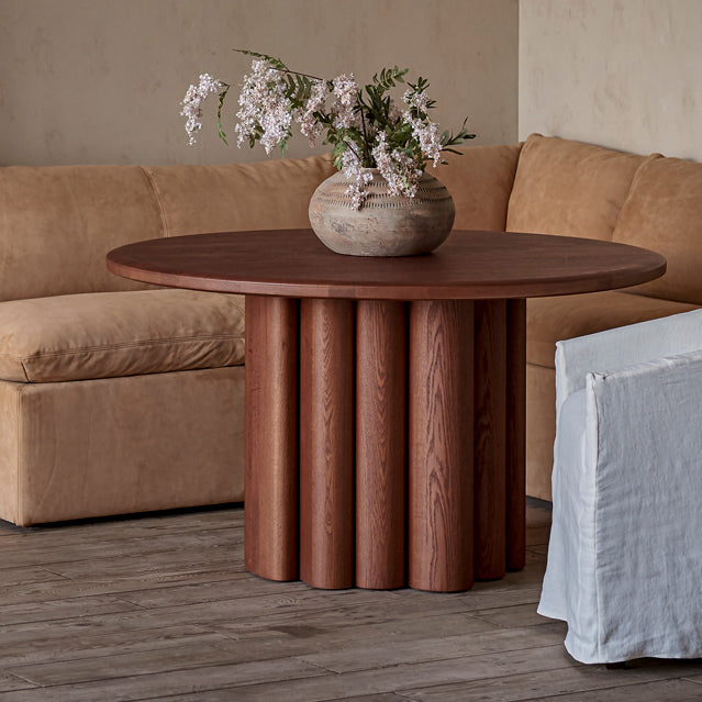 Enzo Dining Table in Spiced Oak, a smokey paprika-hued 100% American red oak, in front of an Aria Leather Banquette in Sunset Canyon
