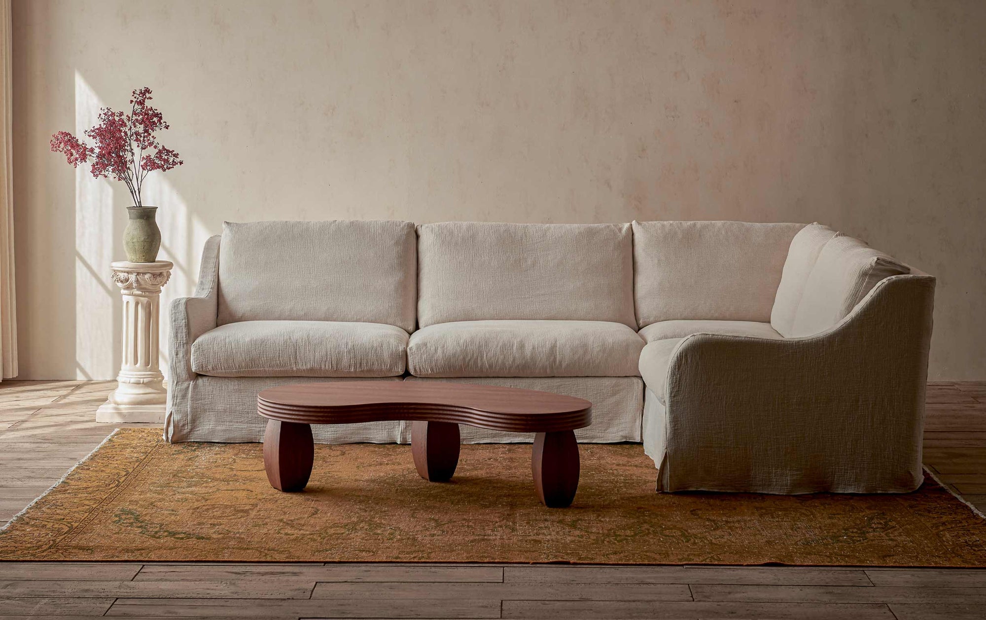 Esmé L-Shape Sectional Sofa in Corn Silk, a light beige Washed Cotton Linen, placed in a sunlit room alongside the Pisces Table