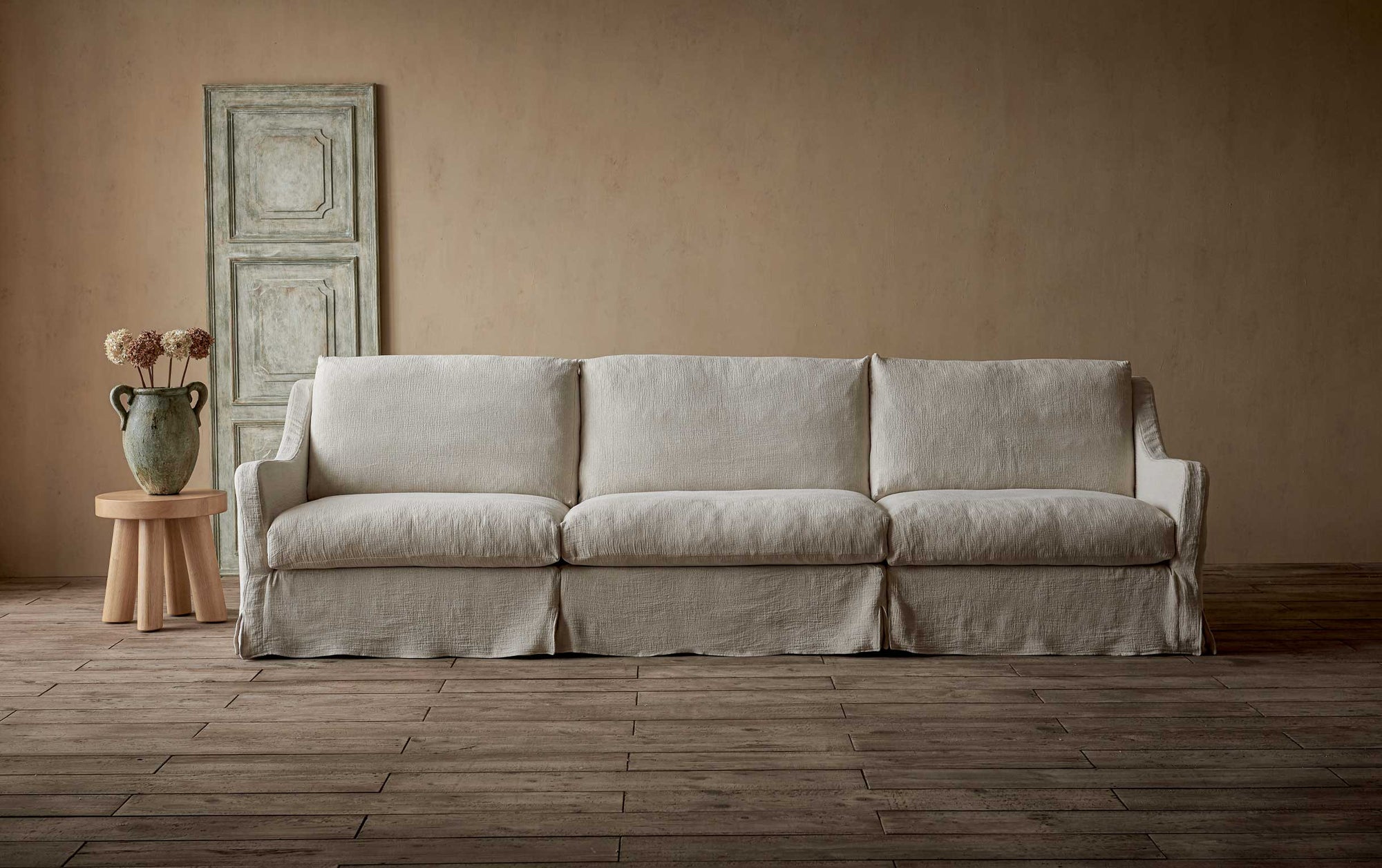 Esmé Sectional Sofa in Corn Silk, a light beige Washed Cotton Linen, next to a side table with a vase of flowers