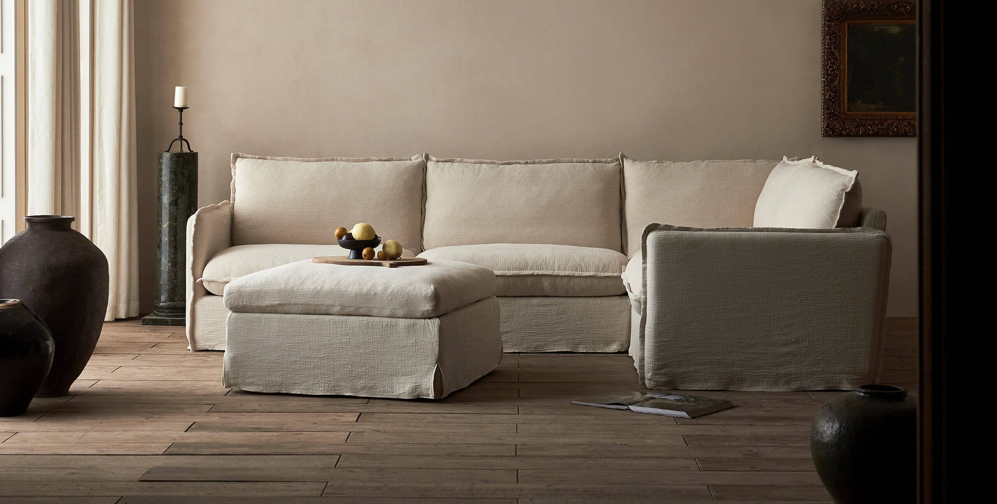 Esmé Storage Ottoman in Corn Silk, a light beige Washed Cotton Linen, in front of a Neva L-Shaped Sectional