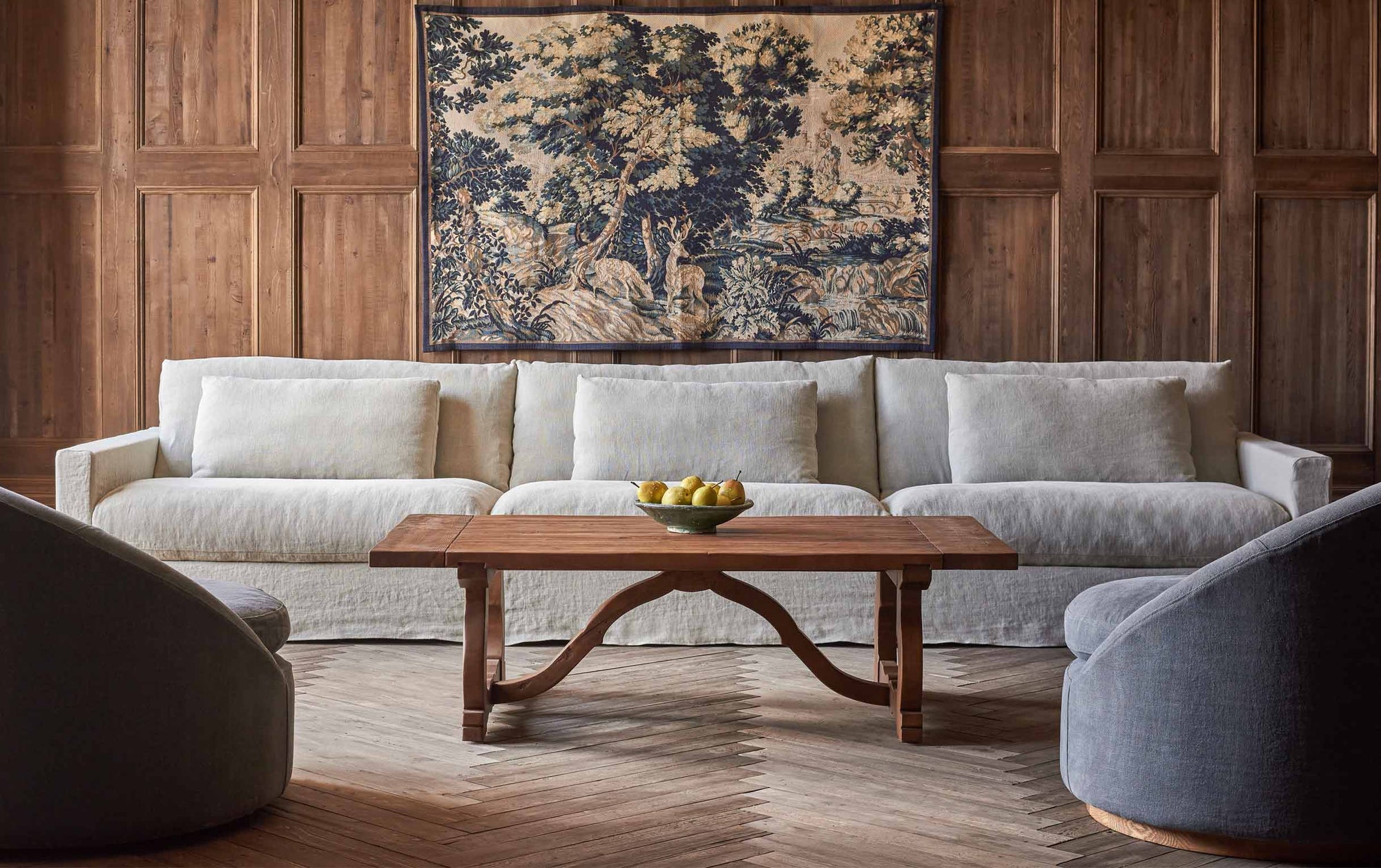 Leona Coffee Table in 100% Reclaimed Chinese Heritage Pine, a medium, bosc pear shade with earthy undertones, placed in a decorated, wood-panelled room surrounded by the Devyn Sectional and two Olea Chairs