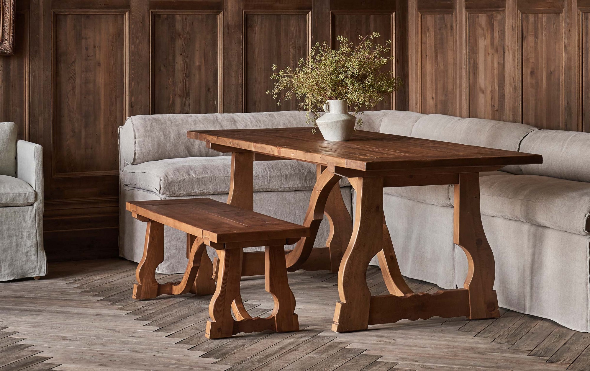 Leona Dining Bench in 100% Reclaimed Chinese Heritage Pine, a medium, bosc pear shade with earthy undertones, placed in a wood paneled room, around a Leona Dining Table with a Camino Banquette