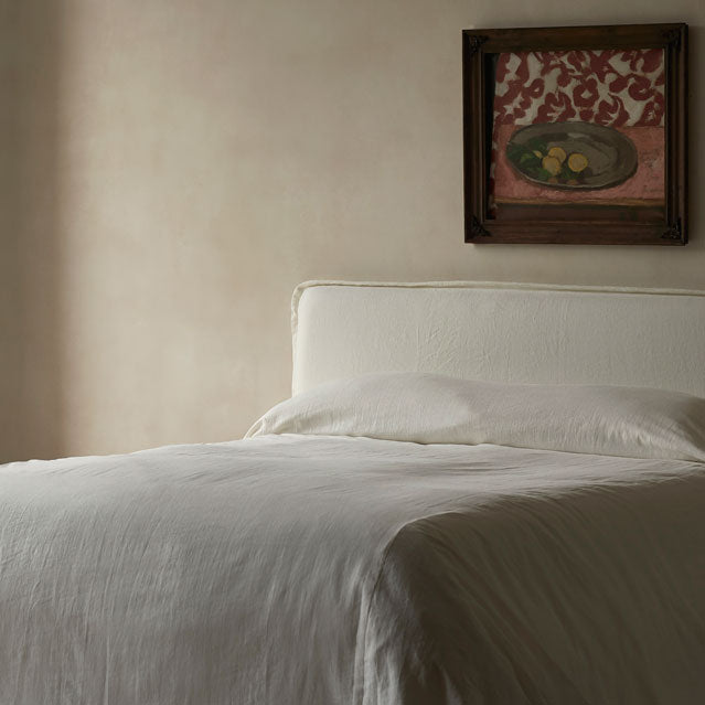 Neva Bed in Water Lily, a white Light Weight Linen with warm undertones, made up with white linen bedding, against a cream wall