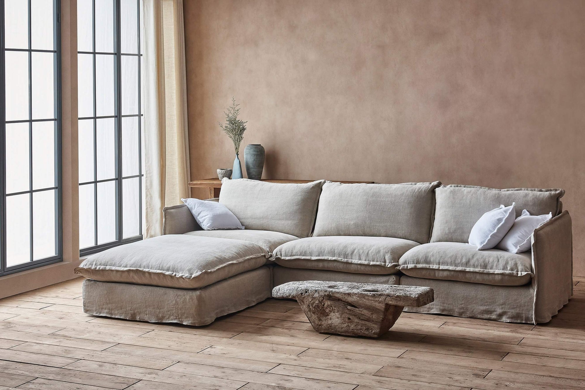Neva 4-piece Chaise Sectional Sofa in Jasmine Rice, a light warm greige Medium Weight Linen, placed in a room next to a window and a coffee table
