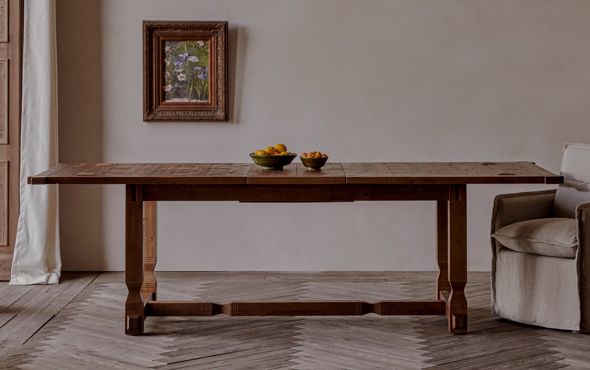Ora Dining Table in 100% Reclaimed Chinese Heritage Pine, a medium, bosc pear shade with earthy undertones, placed in a room with a Melo Dining Chair and a framed painting