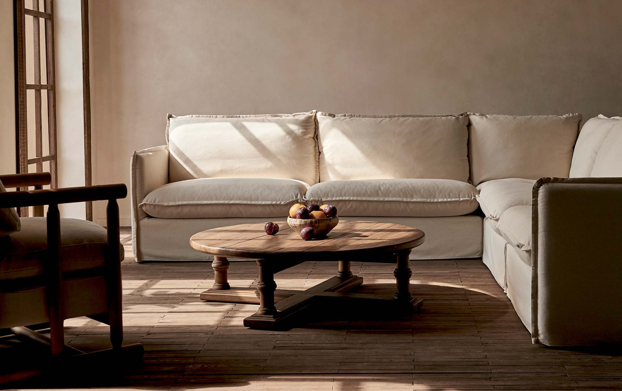 Pia Coffee Table in 100% Reclaimed Chinese Heritage Pine, a medium, bosc pear shade with earthy undertones, decorated with a bowl of fruit and placed in a sunlit room in the middle of a Neva Corner Sectional and a Bene Chair