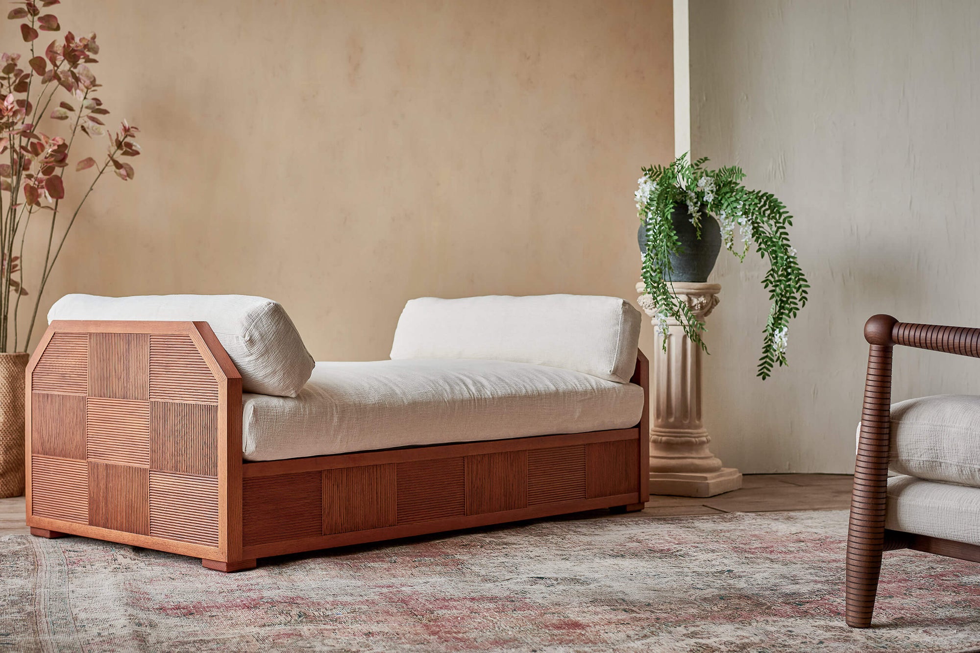 Quincy Daybed with cushions in Corn Silk, a light beige Washed Cotton Linen, placed in a decorated room on a patterned rug with a Gio Chair and flowers on a column