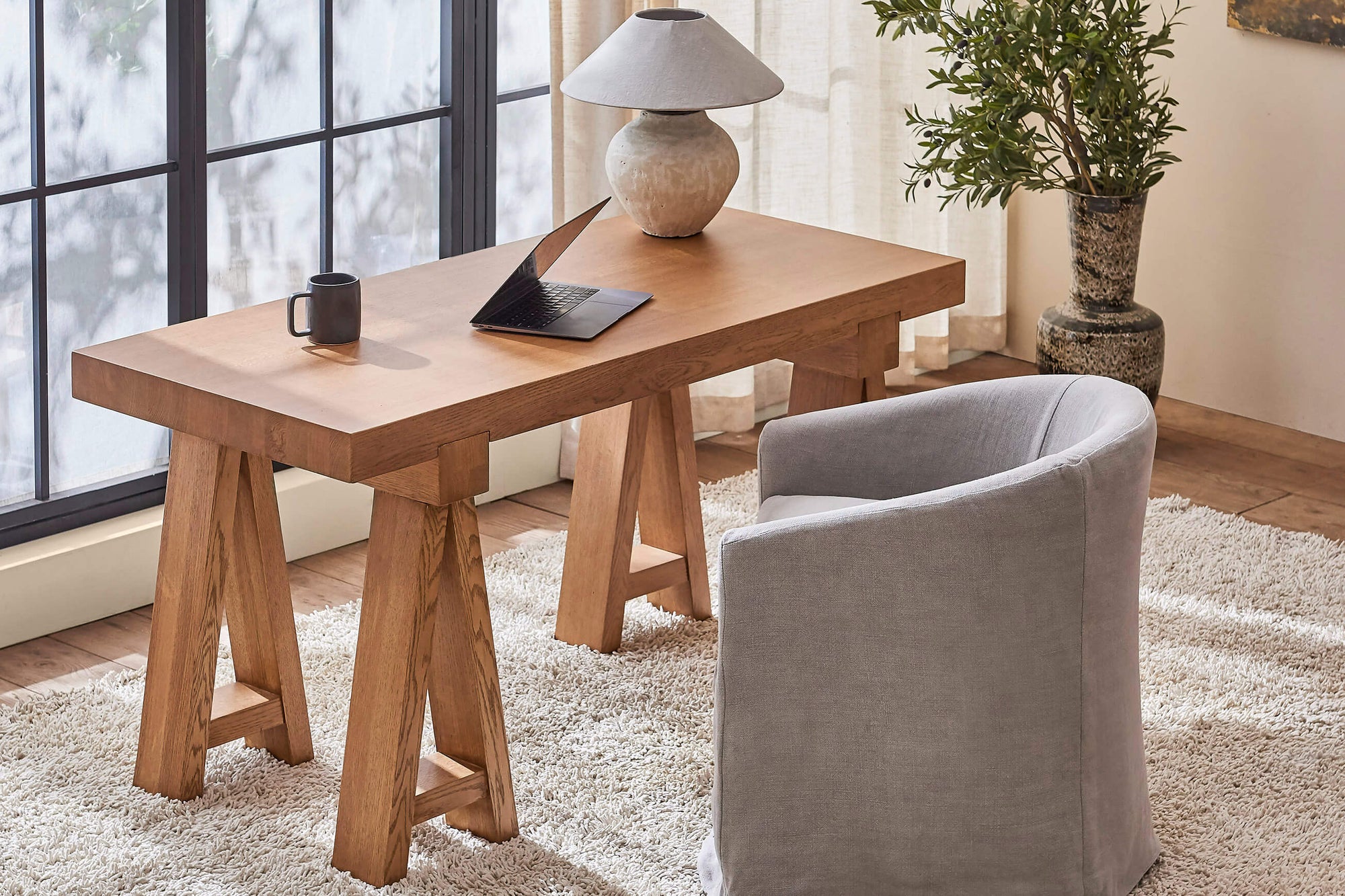 A laptop, lamp, and mug are placed on top of a Rylance Desk in Tinted Oak