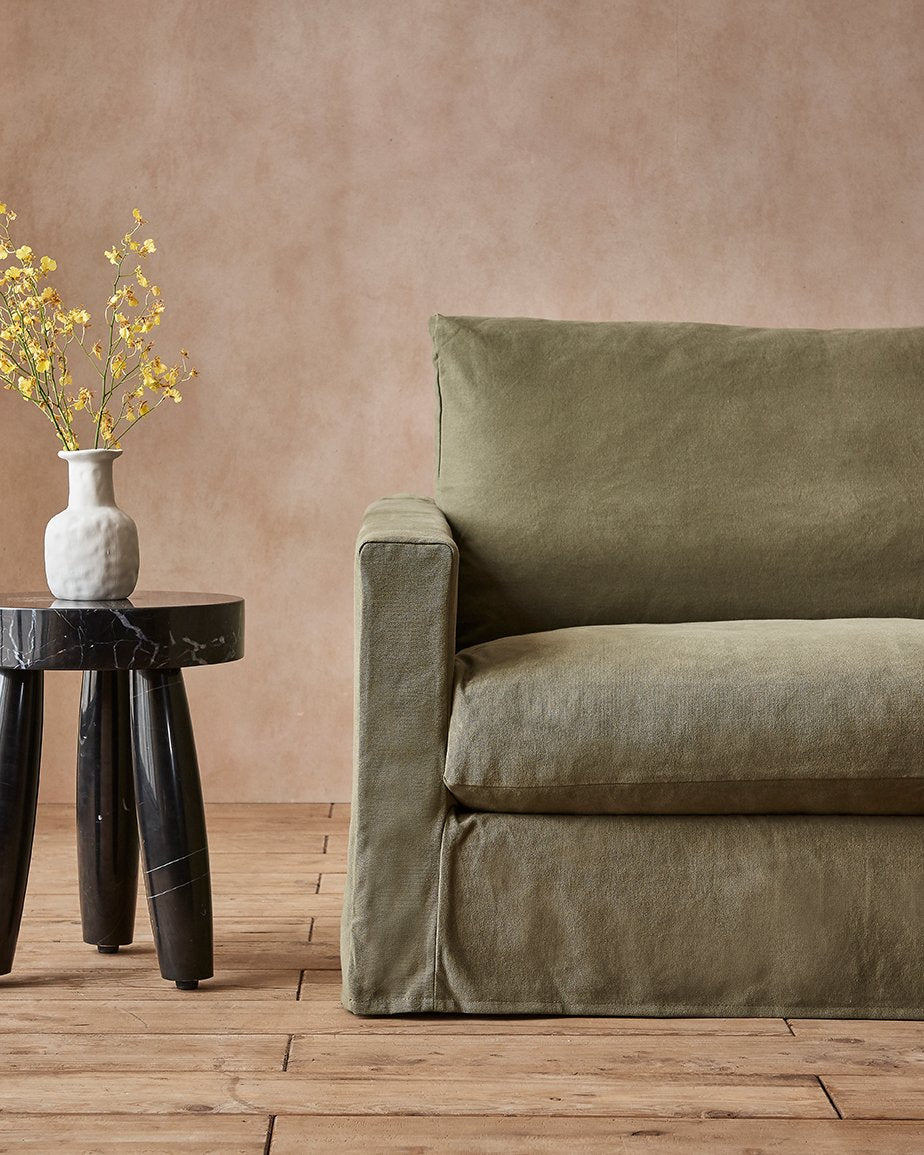 Devyn Sofa in Quiet Sage, an earthy green Cotton Canvas, placed in a room next to a vase of flowers on a stool