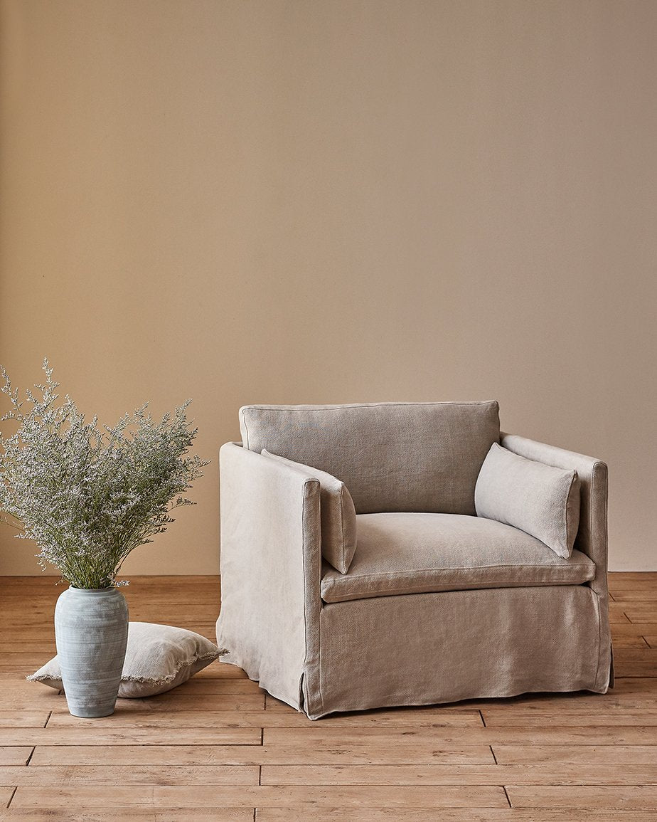 Gabriel Chair in Jasmine Rice, a light warm greige Medium Weight Linen, placed in a room next to a vase of flowering plants on the floor