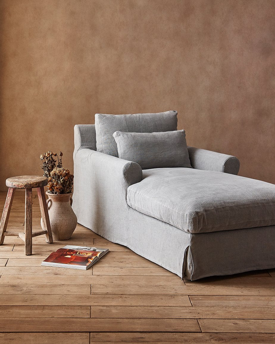 Elias Daybed in Poppy Seed, a light cool grey Medium Weight Linen, placed in a room beside a stool and vase of dried flowers on the floor