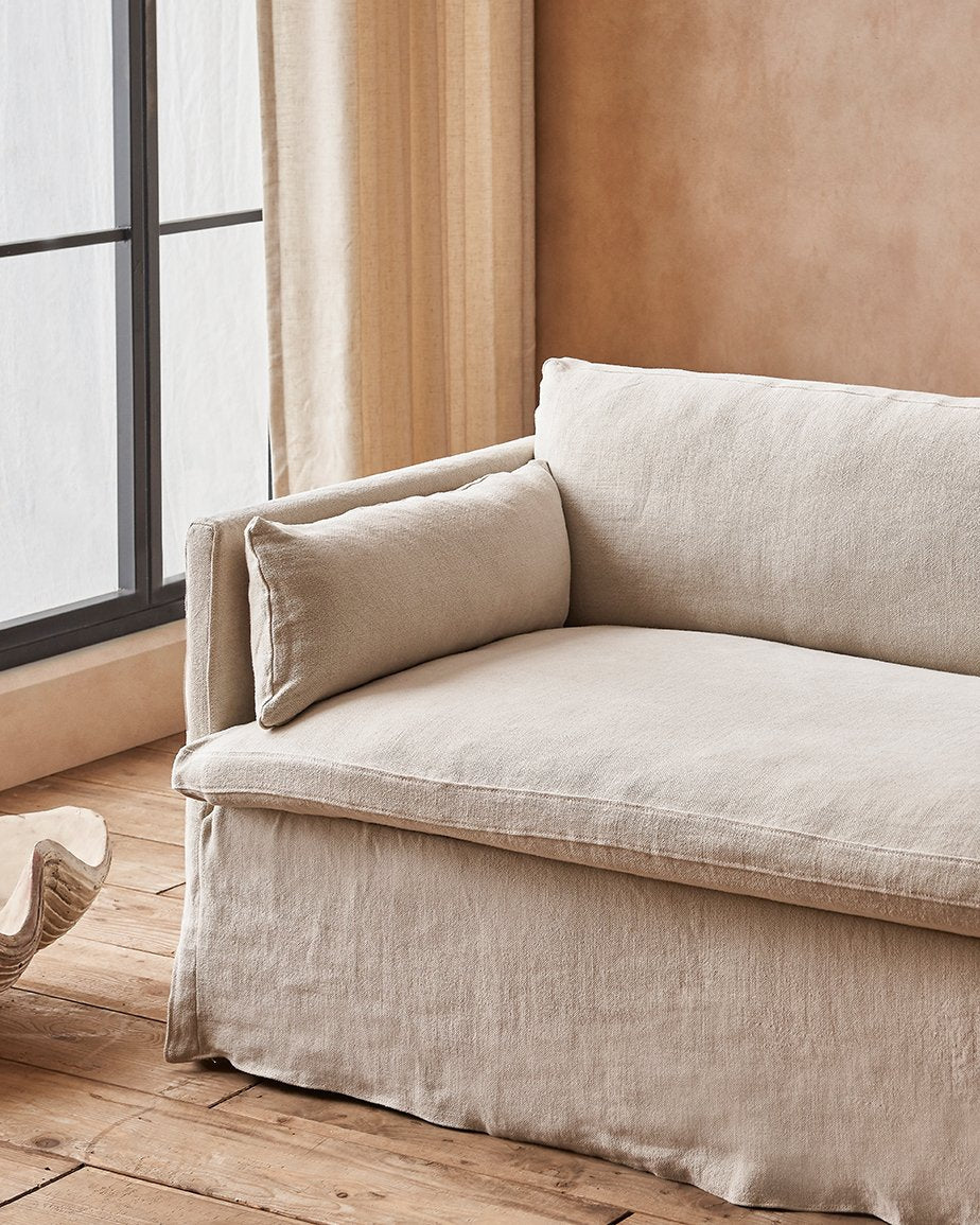 Gabriel Sofa in Warm Oatmeal, a light warm beige Medium Weight Linen, placed in a sunlit room beside the window