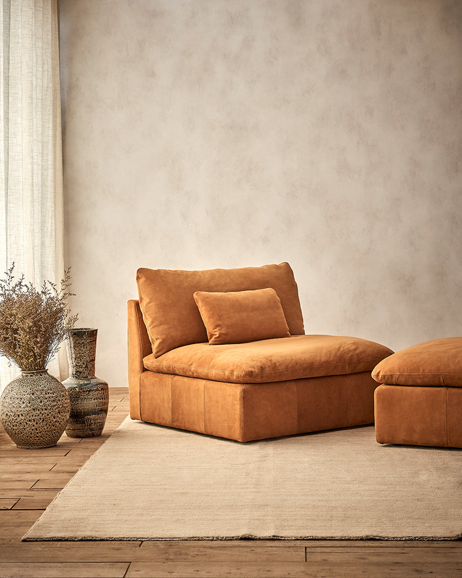 Aria Chair in Sunset Canyon, a cognac brown Meridian Leather, placed in a room with the Aria Leather Ottoman