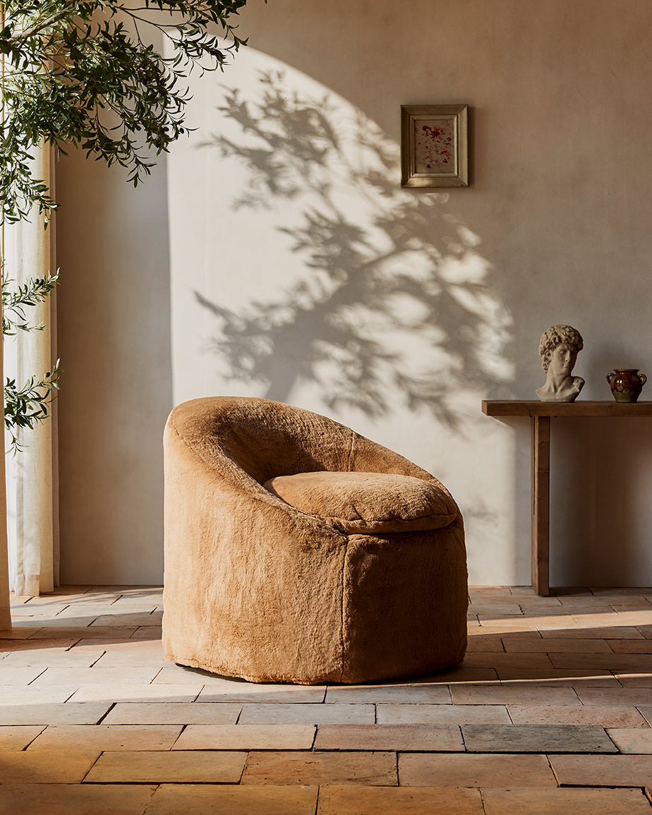 Ozzi Chair in SKiwi Fuzz, a medium golden brown Recycled Faux Fur, placed in a sunlit room with a decorated console table