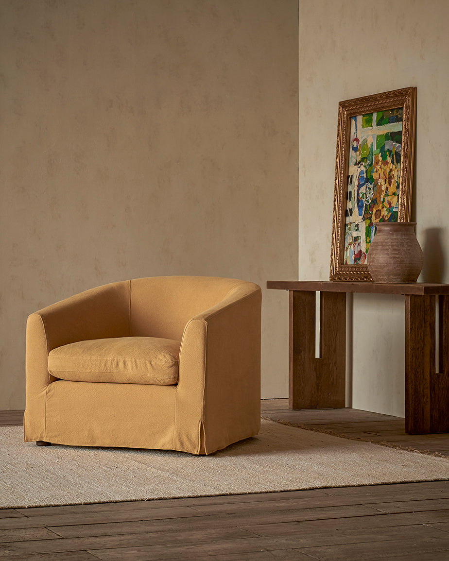 Ziki Chair in  Honey Bee, a saffron yellow Thread-Dyed Cotton Linen, placed in a room in front of a painting and vase on a console table