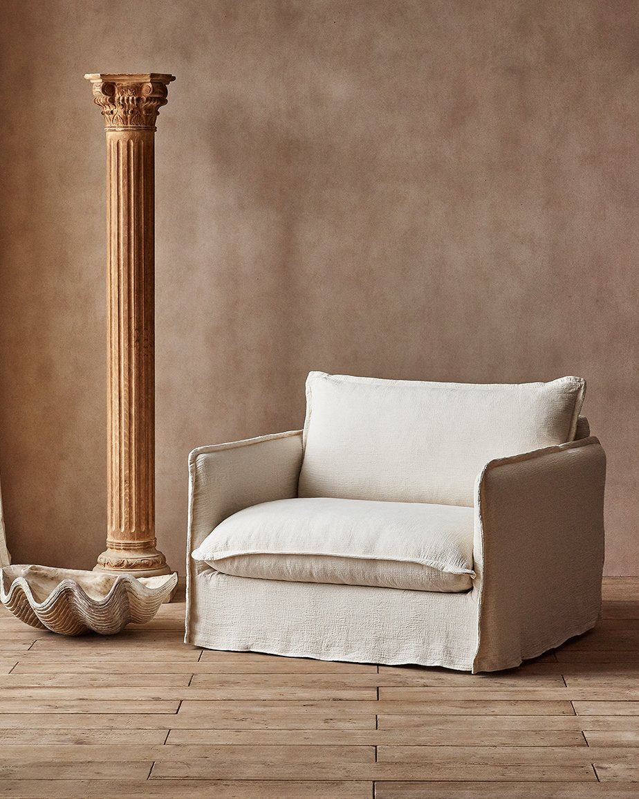 Neva Chair in Corn Silk, a light beige Washed Cotton Linen, placed in a room next to a decorative  pillar