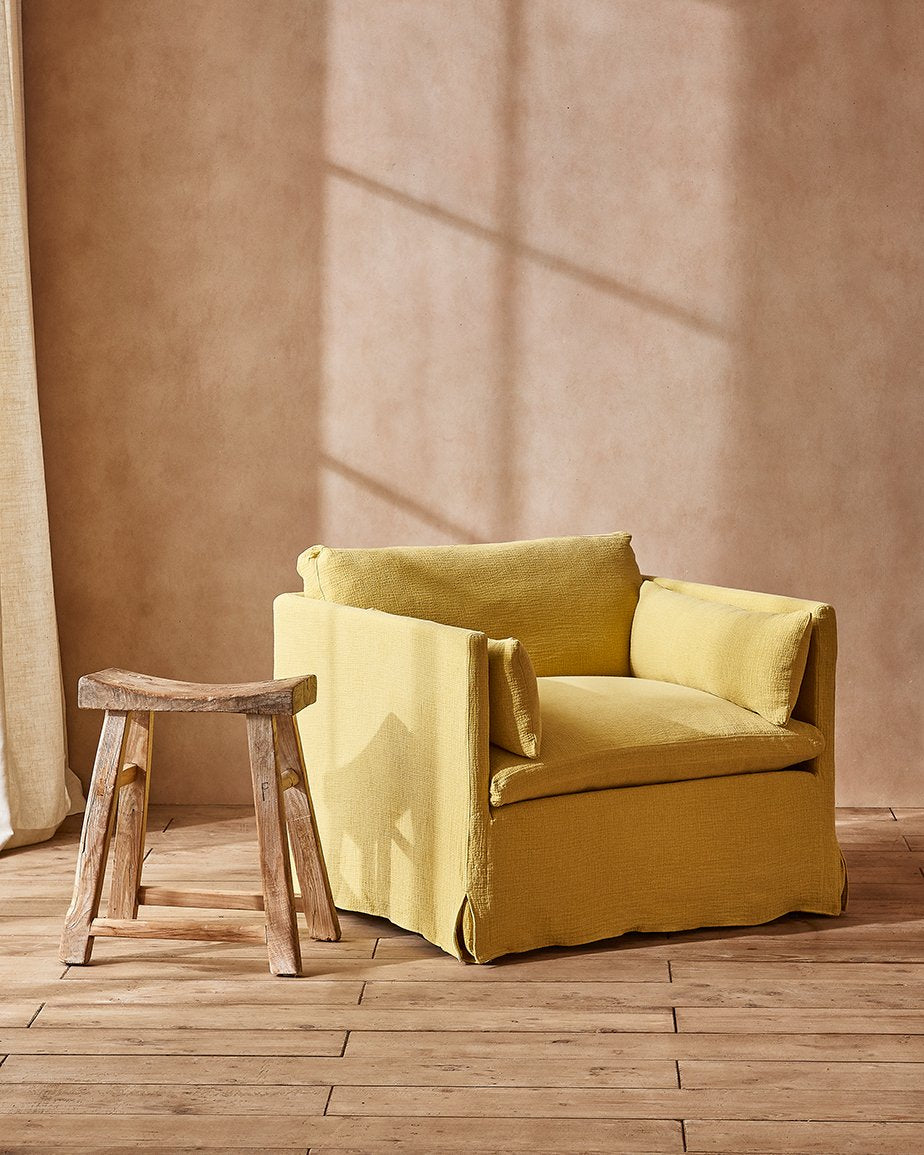 Gabriel Chair in Lemon Ice, a yellow Washed Cotton Linen, placed in a room next to a stool