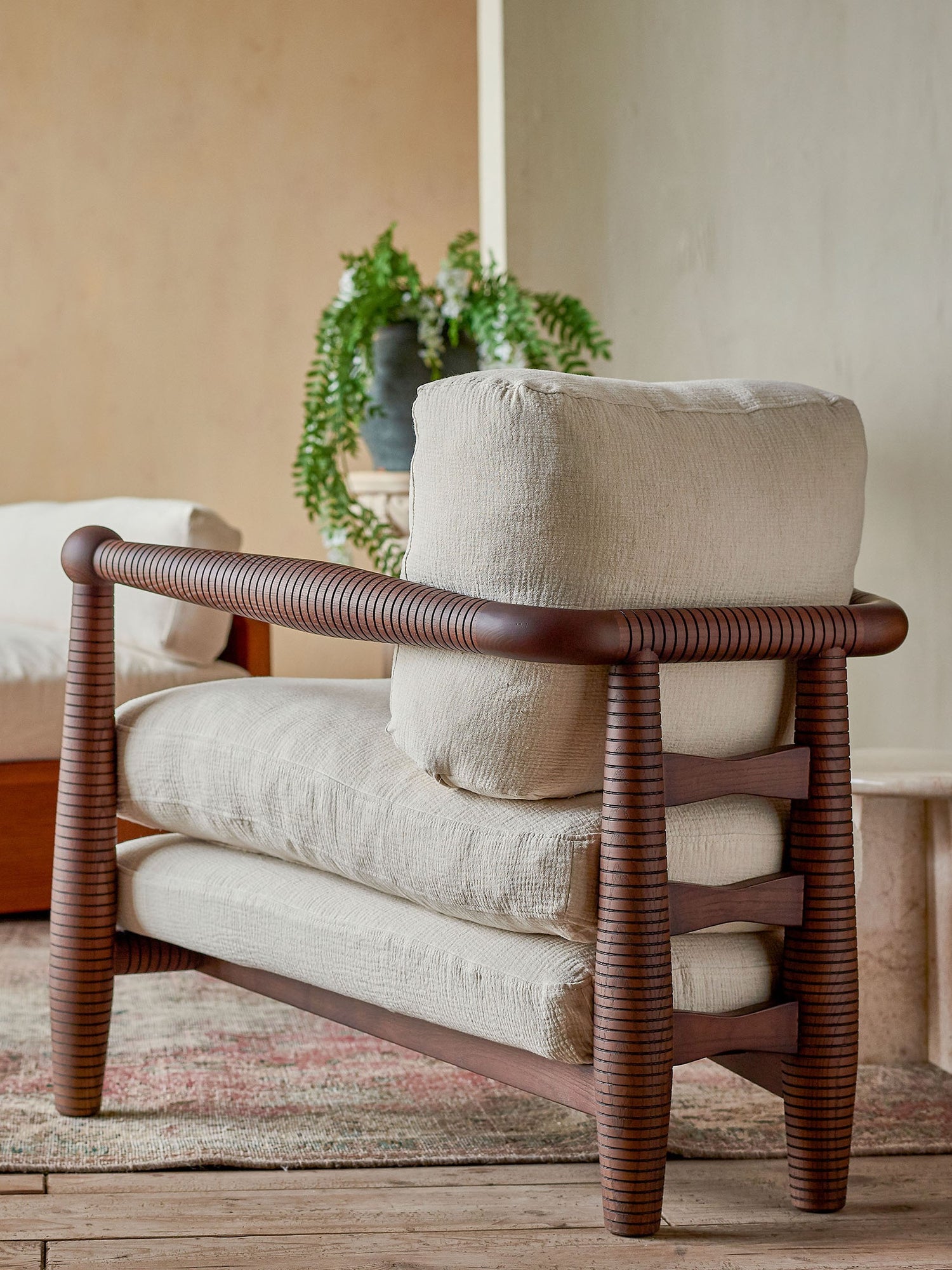 Back view of Gio Chair in Dusky Ash, placed in a sunlit room with a potted plant in background