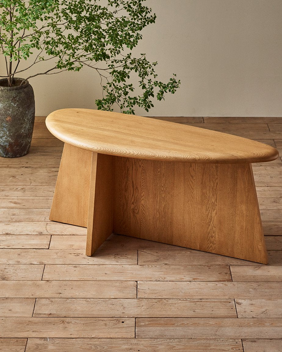 Amina Console Table in Tinted Oak, a golden, wheat-colored 100% American red oak, placed in a room in front of a potted tree