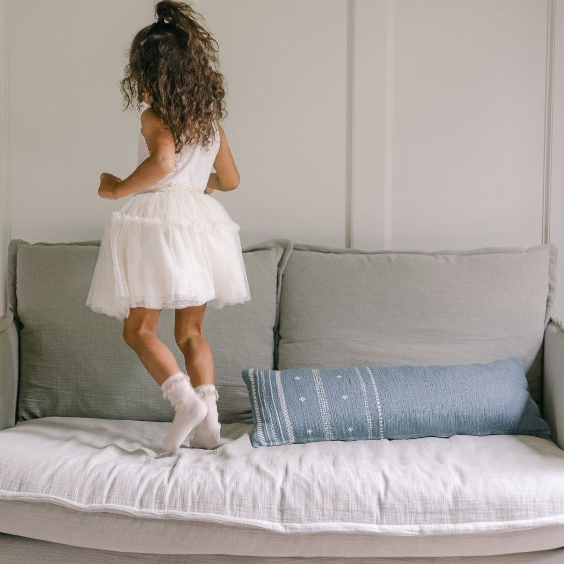 a young girl standing on top of the Neva Loveseat in Jasmine Rice, Medium Weight Linen