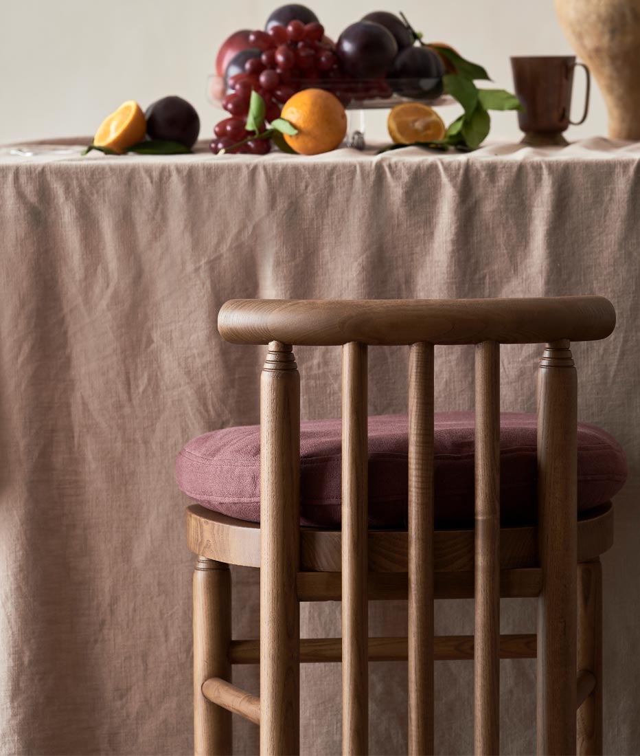 Bene Dining Chair in Heritage Ash and Summer Plum cushions placed next to a table with fruits on the tabletop