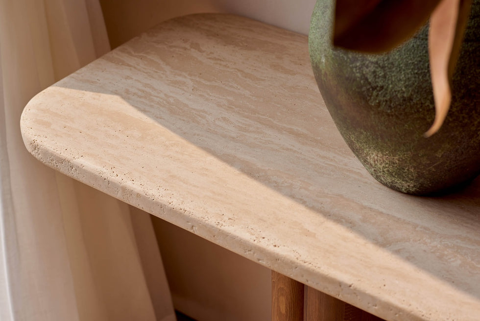 Close up of Enzo Console Table in Turkish Galata Travertine in a warm beige with gold and pink undertones. Various veining, color variations, and pitting throughout. The console is topped with a green vase.