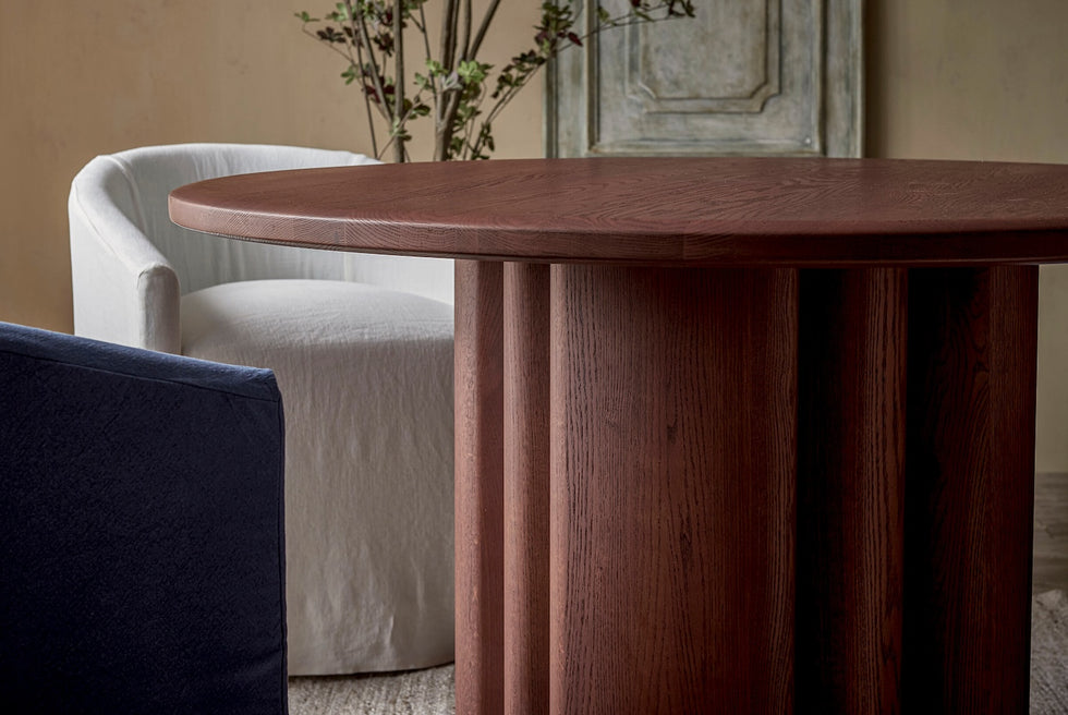 Enzo Round Dining Table in Spiced Oak, a smokey paprika-hued 100% American red oak, placed in a decorated room with Ziki Dining Chairs