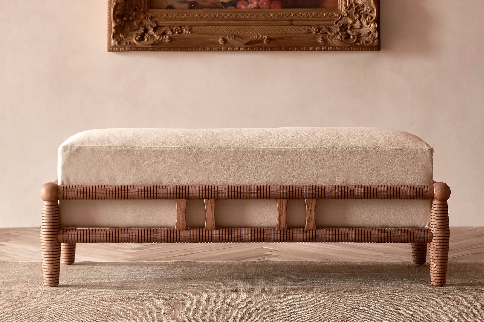 Gio Dining Bench in a Heritage Ash wood frame with Cotton Canvas Beach Walk slipcover, placed on top of a rug