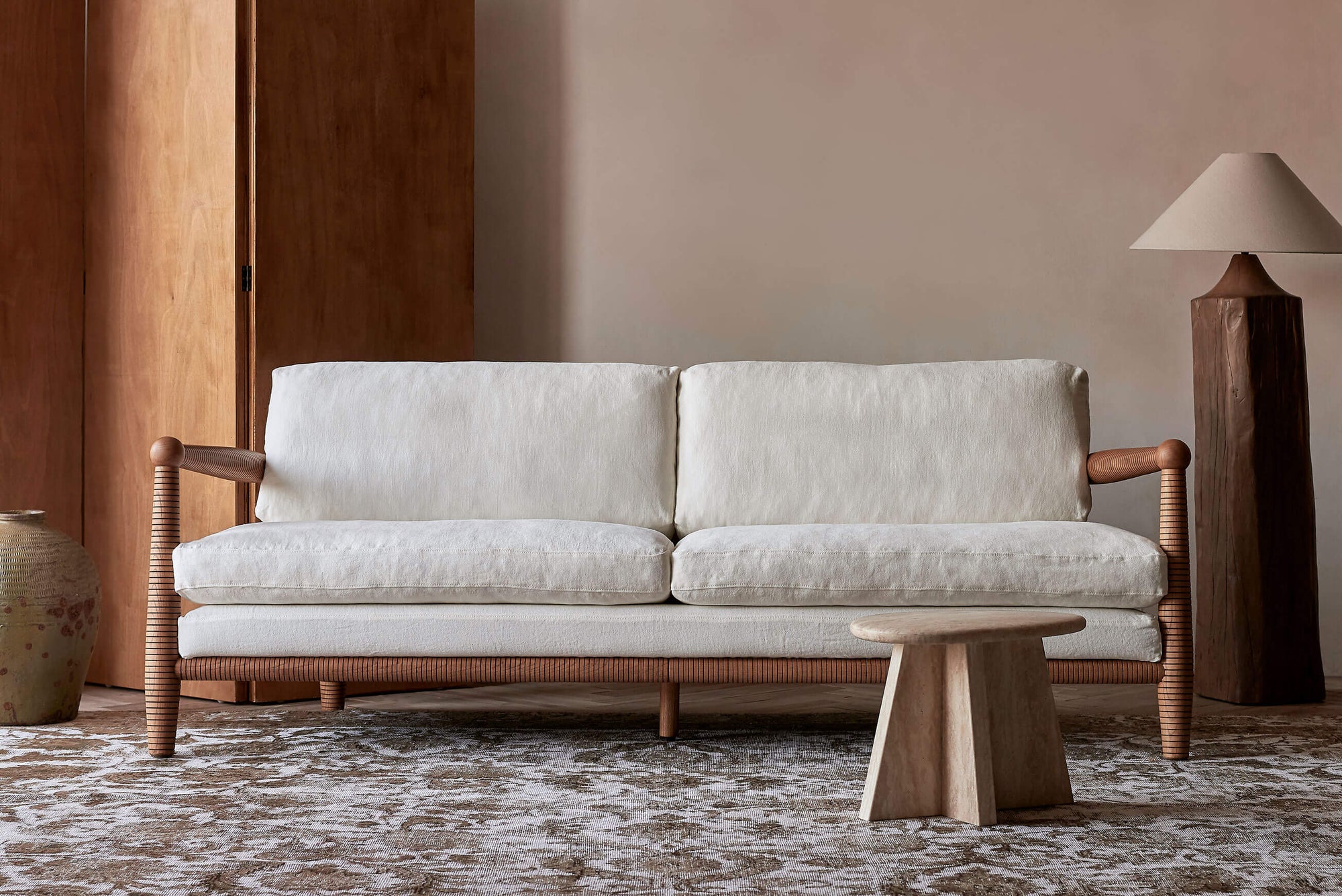 Gio 84" Sofa in a Heritage Ash wood frame with Light Weight Linen Water Lily slipcover, placed in a room with decorative pillars and side tables
