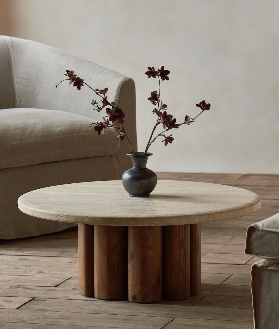 A vase with flowers is placed on the surface of the Enzo Coffee Table in Galata Travertine and Heritage Pine
