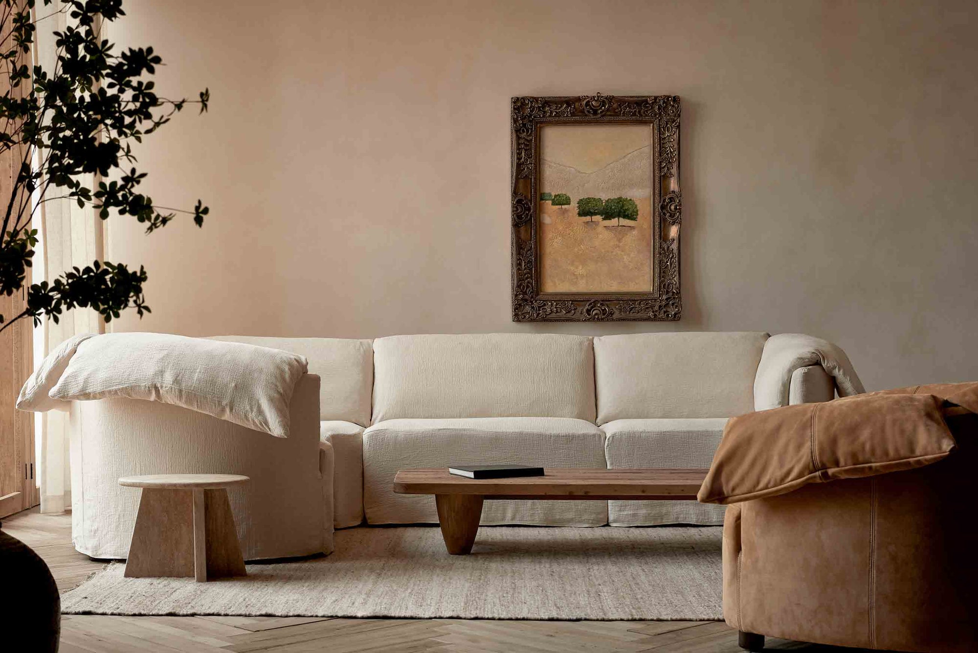 Loula L-Shape Sectional in Corn Silk, a light beige Washed Cotton Linen, placed in a living room with a Theo Coffee Table, decorative side table, and Loula Leather Chair