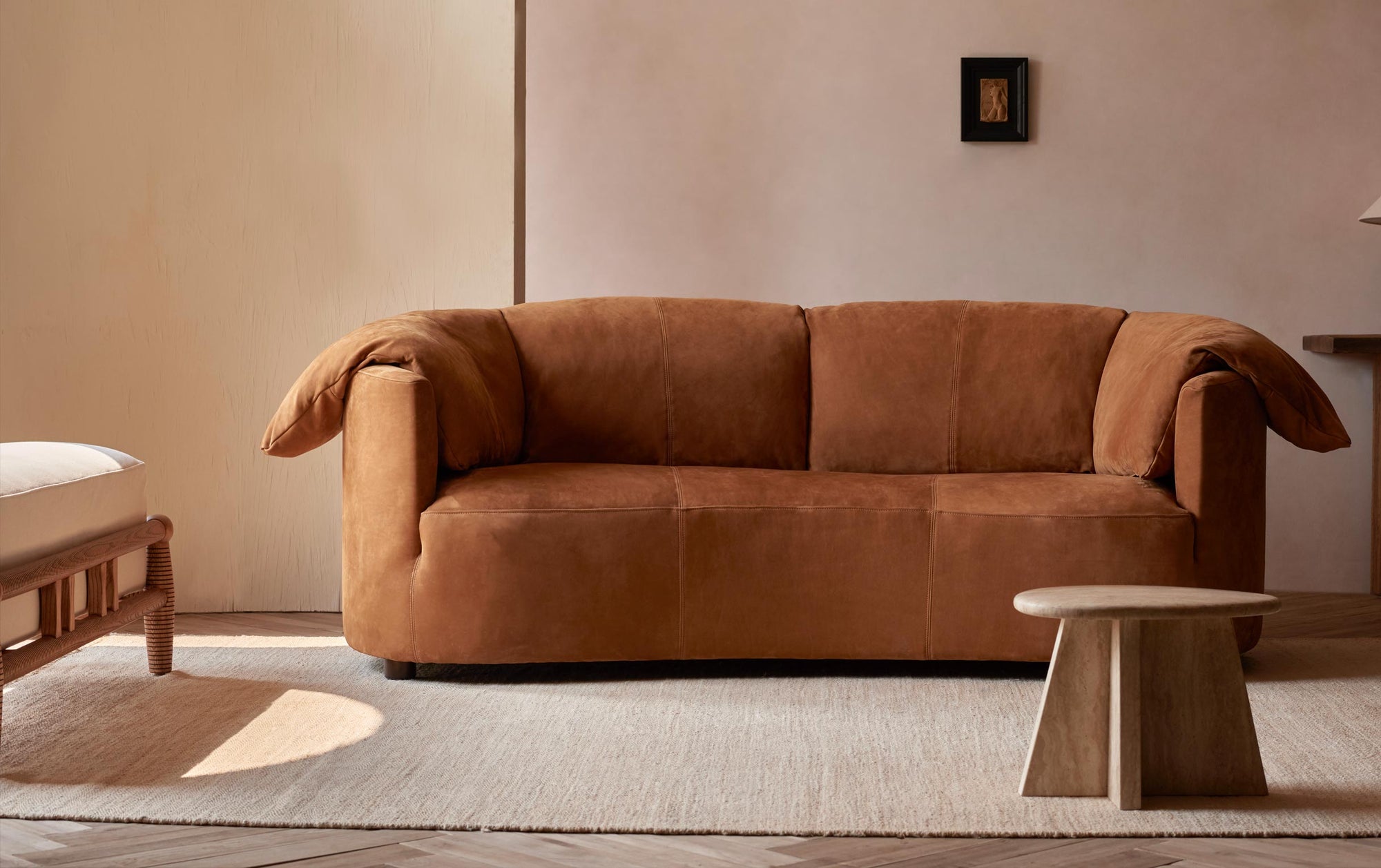 Loula Leather Sofa in Sunset Canyon, a cognac brown Meridian Leather, on a creamy beige carpet with a wooden side table
