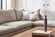 Slide #6 Close up of Amelia Corner Sectional Sofa in Jasmine Rice, a light warm greige Medium Weight Linen, placed around a Kai Coffee Table holding books and thing purple vase