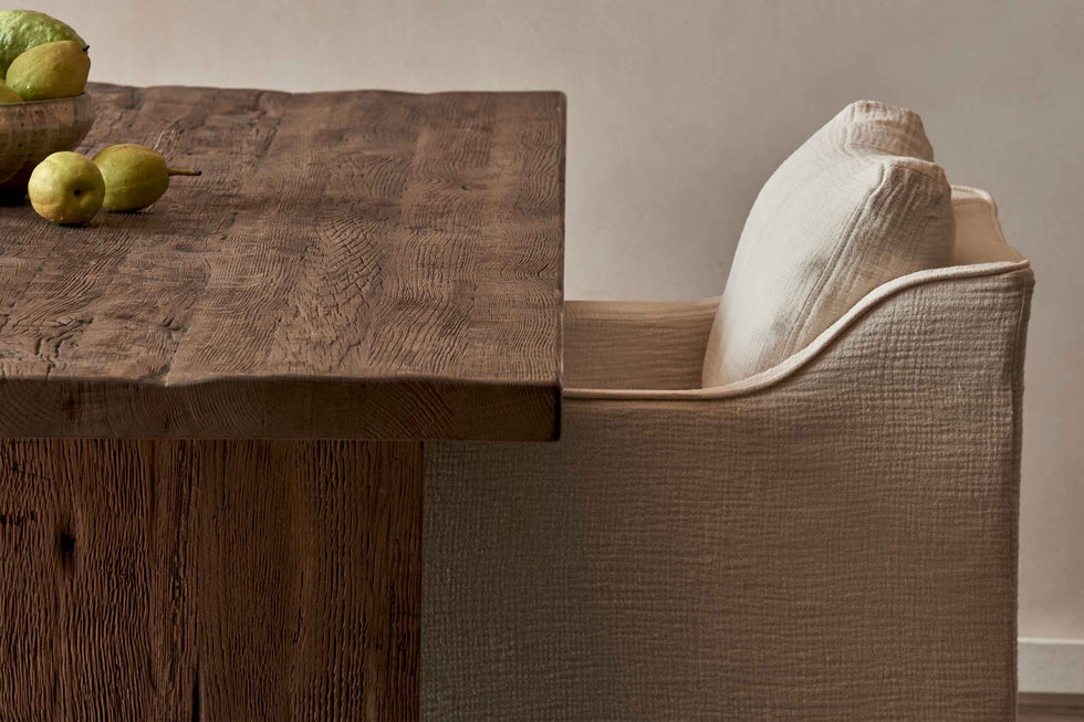 Close up of Amelia Dining Chair in Corn Silk, a light beige Washed Cotton Linen, placed at a Kai Dining Table topped with pears